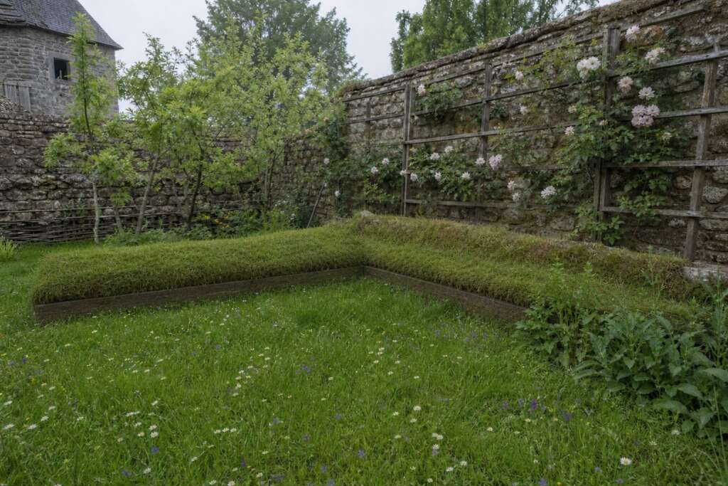 Reconstruction of a late-medieval enclosed garden with an L-shaped turf seat, rose trellis, fruit trees, and flowering grass.