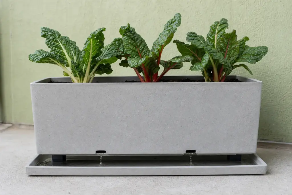 Low side view of a rectangular balcony planter raised above a shallow catch tray, with fresh runoff beneath the drainage holes.